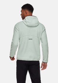 Mintgrünes Fleece-Jacke mit Kapuze, featuring einer strukturierten Oberfläche und schwarzen Akzenten, Markenlogo auf dem Rücken und einer lässigen Passform.