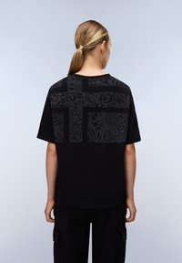 Černé bavlněné tričko s texturovaným grafickým designem v šedé na zadní straně. Kulatý výstřih, krátké rukávy a volný střih.