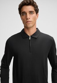 Czarny polo z długim rękawem i zamkiem przy dekolcie, wykonany z gładkiego materiału. Posiada tradycyjny kołnierz i dopasowane rękawy.