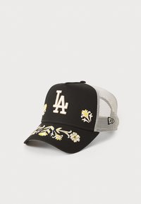 Svart keps med en krämfärgad "LA"-logotyp, blommig broderi i gult och vitt, samt en grå mesh-bak. Böjd skärm, strukturerad krone.