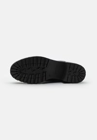 Sole in gomma nera con un motivo di scolpitura profonda, caratterizzata da creste e scanalature per garantire aderenza. Logo del marchio impressa sul lato. Materiale resistente.
