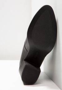 Botte en cuir noir avec une finition lisse, un embout carré et une semelle en caoutchouc texturée. Le talon est épais et légèrement surélevé.