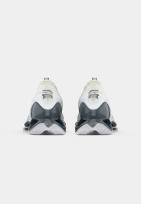 Athletic shoes featuring a white upper with gray accents, textured finish, and a thick, translucent sole with deep treads.