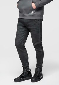 Jeans gris foncé à coupe slim, avec un design cinq poches et des détails subtils de décoloration. Associés à des baskets noires montantes.