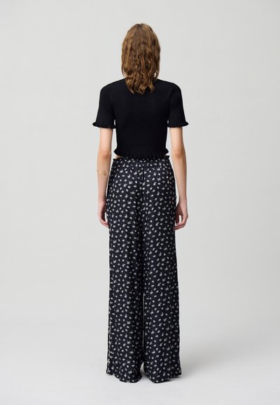 Top negro de manga corta con textura acanalada, combinado con pantalones largos de tiro alto y pernera ancha en negro, con un patrón floral blanco y aberturas laterales.