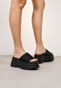 Zapatos de plataforma negros con correas anchas de acabado mate y una suela texturizada y gruesa. La suela presenta surcos profundos para mayor agarre y estabilidad.