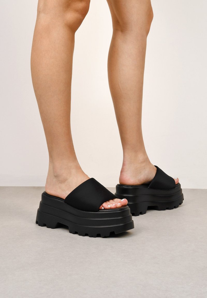 Zapatos de plataforma negros con correas anchas de acabado mate y una suela texturizada y gruesa. La suela presenta surcos profundos para mayor agarre y estabilidad.