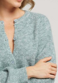 Cardigan en tricot bleu clair avec une texture côtelée, doté de boutons ronds gris et d'un décolleté en V profond. Apparence douce et confortable.