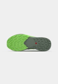 Semelle de chaussure avec une bande de roulement en caoutchouc vert et gris présentant des motifs géométriques et un petit logo triangulaire rouge au centre.