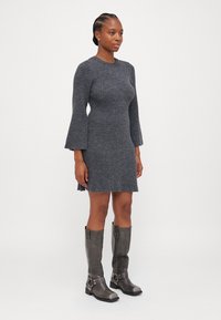 Robe tricotée grise à rayures avec des manches évasées et des fentes latérales, associée à des bottes en cuir gris foncé allant jusqu'aux genoux avec des accents de bride autour de la cheville.
