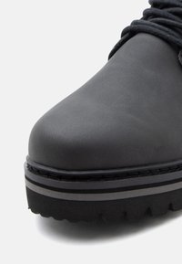 Primo piano di un stivale platform nero con suola spessa, due strisce orizzontali sulla suola intermedia e lacci neri.