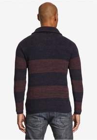 Maglione a righe blu scuro e bordeaux con colletto a scialle, texture a costine e maniche lunghe, indossato sopra jeans grigi.