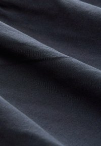 Tela negra con una textura suave y un sutil estriado, drapeada para mostrar suaves pliegues y variaciones en las reflexiones de la luz.