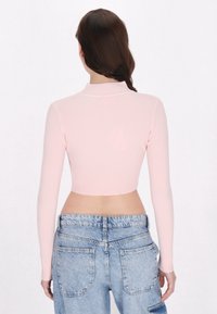 Helles rosa, geripptes Langarm-Crop-Top mit hohem Kragen, kombiniert mit hochgeschnittenen Acid-Wash-Jeans, die auffällige Gesäßtaschen aufweisen.