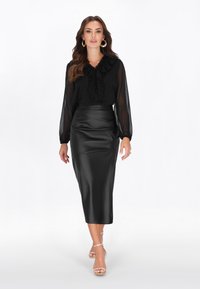 Fekete áttetsző blúz fodros nyakkivágással, fekete selyem ceruzaszoknyával és áttetsző pántos magassarkúval párosítva. Selymes anyagok, testhez simuló szabás.
