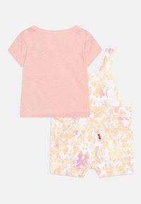 Różowa koszulka z krótkim rękawem zestawiona z żółtymi, pomarańczowymi i różowymi ogrodniczkami w stylu tie-dye, które mają dwie tylne kieszenie i regulowane ramiączka.