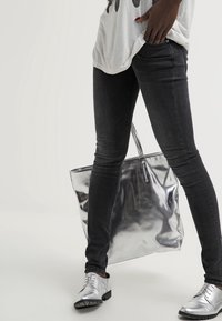 Silver tote bag with reflective surface, worn with dark skinny jeans and metallic silver shoes. Grey graphic tee completes the outfit.