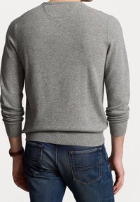 Pull gris en maille avec manches longues et poignets côtelés, associé à un jean bleu foncé avec deux poches arrière et des coutures contrastantes.