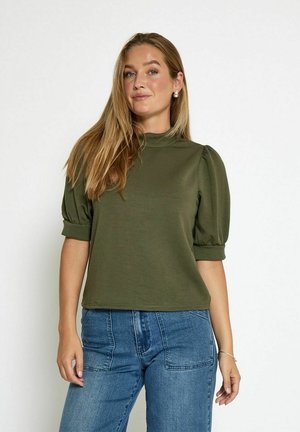 Olive green short-sleeve top with puffed sleeves, high neckline, and a relaxed fit. Paired with blue denim jeans.