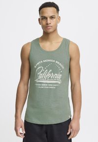 Zeleni top s okruglim izrezom i ležernim krojem, s bijelim grafičkim natpisom "Santa Monica Beach California."