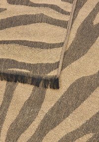Tessuto intrecciato marrone e beige con un motivo a strisce zebra e un bordo frangiato, piegato su una superficie con motivo coordinato.