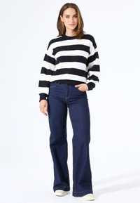 Gestreifter Pullover in Schwarz und Weiß mit geribbelter Textur, kombiniert mit dunkelblauen Schlagjeans und hellen Sneakern.