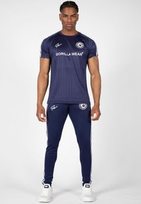 Marineblauwe sportt-shirt met verticale strepen en het "Gorilla Wear" logo, gecombineerd met bijpassende joggingbroeken met zijstrepen en logo-accenten.