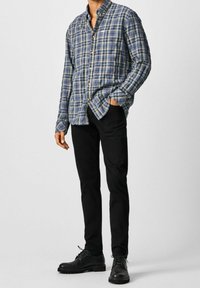 Camisa de cuadros azul y verde con botón y mangas largas, combinada con jeans negros ajustados y botas negras con cordones.