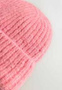 Różowy wełniany czapka z miękką, puszystą teksturą i prążkowanym wzorem. Okrągły szczyt i widoczne szwy, idealna na zimne dni.