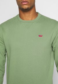 Grön långärmad sweatshirt i mjukt, texturerat tyg med rund halsringning. Har en röd Levi's-logotyp på vänster bröst.