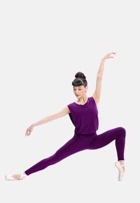 Purple athletic outfit with a loose top and form-fitting leggings, paired with pink ballet shoes. Model poses in an extended dance stance.