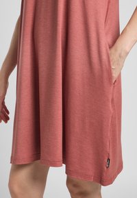 Kurzärmliges, knielanges Kleid aus einem weichen, melierten Korallestoff mit seitlichen Taschen und einem dezenten Markenetikett am Saum.