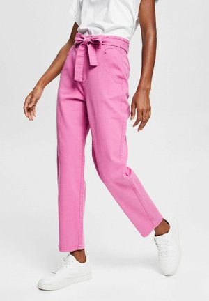 Rosa denimbyxor med knytmidja, sidofickor och en avslappnad passform, tillsammans med vita sneakers mot en neutral bakgrund.