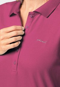 Paars poloshirt met een kraag, twee knopen en een klein zilveren geborduurd detail. Katoenen materiaal, gladde textuur. Close-up weergave.