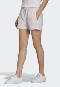 Zachtroze katoenen shorts met een elastische tailleband en zijzakken, met een subtiele logo op de voorkant. Gestyled met witte sneakers.