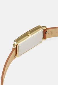 Zlatý hodinky s obdélníkovým pouzdrem, hladkým stříbrným zadním víčkem a hnědým koženým páskem. Obsahuje boční korunku pro nastavení.