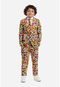 Completo colorato per bambini realizzato in tessuto con un motivo di grandi cerchi in rosa, blu, verde e giallo, con una cravatta abbinata e una camicia bianca.