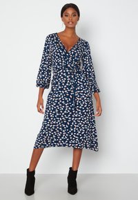 Granatowa sukienka w kwiaty z długimi, bufiastymi rękawami, dekoltem w kształcie litery V i wiązaniem w talii. Posiada białe i różowe wzory kwiatowe.