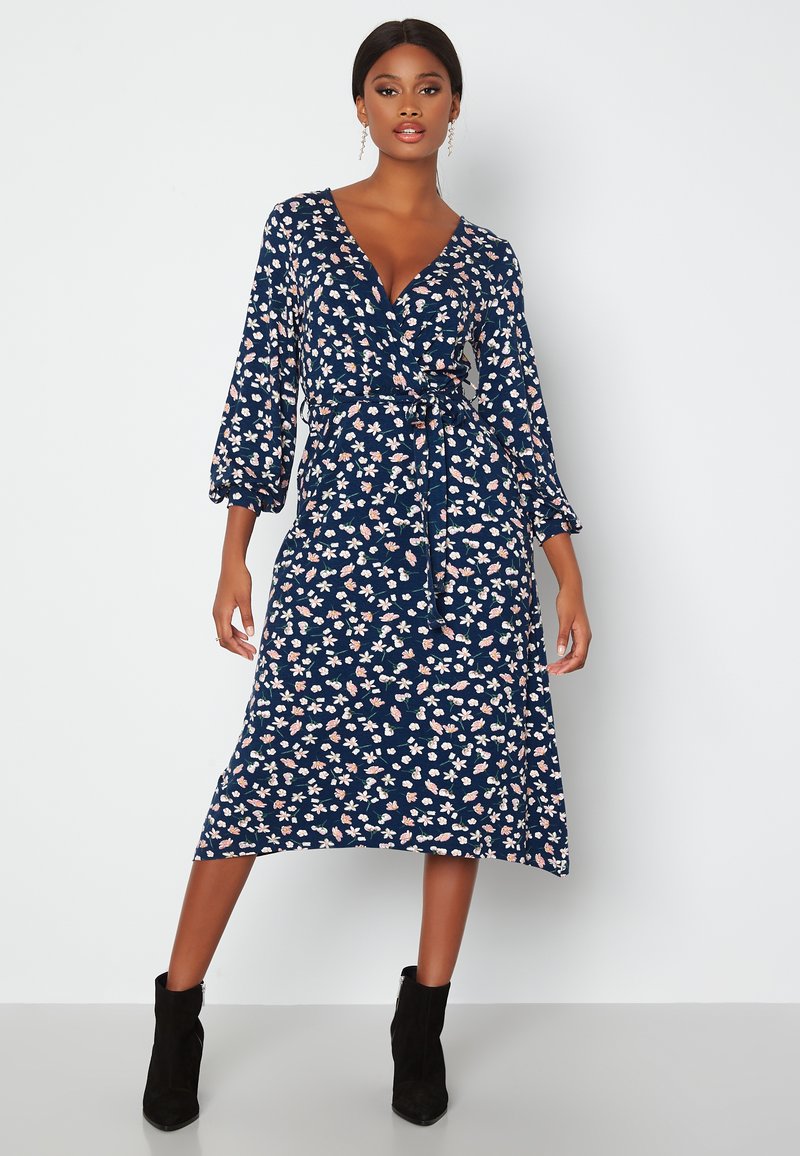 Granatowa sukienka w kwiaty z długimi, bufiastymi rękawami, dekoltem w kształcie litery V i wiązaniem w talii. Posiada białe i różowe wzory kwiatowe.