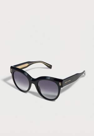 Czarne, duże okulary przeciwsłoneczne w stylu kociego oka z gradientowymi ciemnymi soczewkami i logo Marc Jacobs na zauszniku, prezentowane na białym tle.