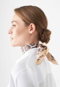 Foulard en soie avec un imprimé léopard dans des tons de marron et beige, noué autour du cou d'une personne portant une chemise blanche, montrant des détails de texture et de motif.