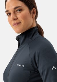 Giacca zip-up Vaude in grigio scuro, in tessuto textured con colletto alto, caratterizzata da dettagli del logo in bianco sul petto e sulla manica.