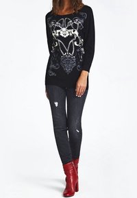 Zwarte langemouwtop met witte grafische print, gecombineerd met donkerdenim jeans en rode enkellaarzen met ritssluiting.