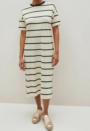 Kobieta w kremowej sukience midi z czarnymi poziomymi paskami i krótkimi rękawami, zestawiona z metalicznymi sneakersami na platformie w kolorze różowego złota.