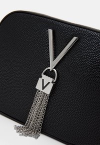 Black textured clutch with silver V-shaped metal detail and tassel chains hanging from a square metal piece with a V engraving.