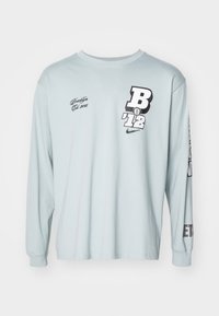 Helles blaues Langarm-T-Shirt aus Baumwolle. Mit grafischen Drucken: "B '12" und "Brooklyn" in Schwarz. Crew-Ausschnitt, lockere Passform, gerippte Bündchen.