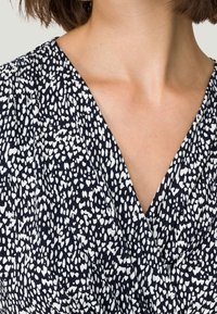 Robe marine avec un col en V, des manches courtes et un motif texturé de speckles blancs et de formes irrégulières sur le tissu.