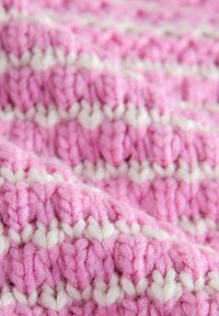 Primo piano di un tessuto spesso lavorato a maglia con filato rosa e bianco alternato in righe orizzontali.