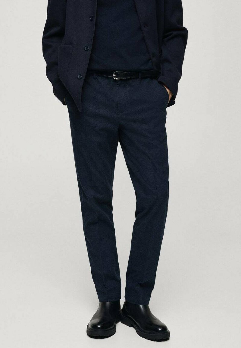 Pantaloni blu con un tessuto testurizzato, design affusolato, tasche laterali, abbinati a un blazer blu coordinato e stivali neri lucidi.