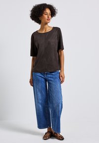 Top corto manica corta in suede marrone con scollo rotondo, abbinato a jeans larghi in denim blu e scarpe basse con stampa leopardata.